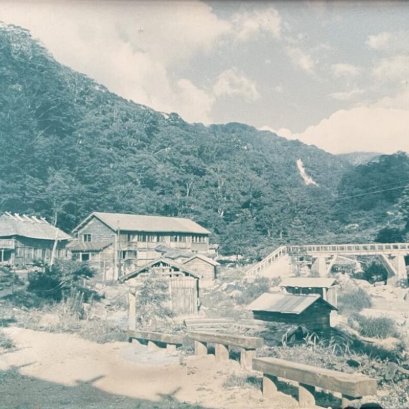 孫六温泉（昭和40年代） 先達川に架かる橋の先にある自炊部と旅館部。川側には温泉小屋が点在している。